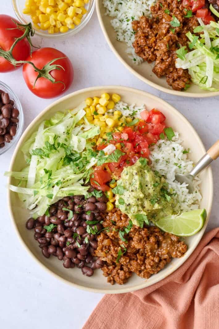 Best ground beef burrito bowls loaded with all the toppings, including lettuce, black beans, corn, rice, tomatoes, and guacamole.