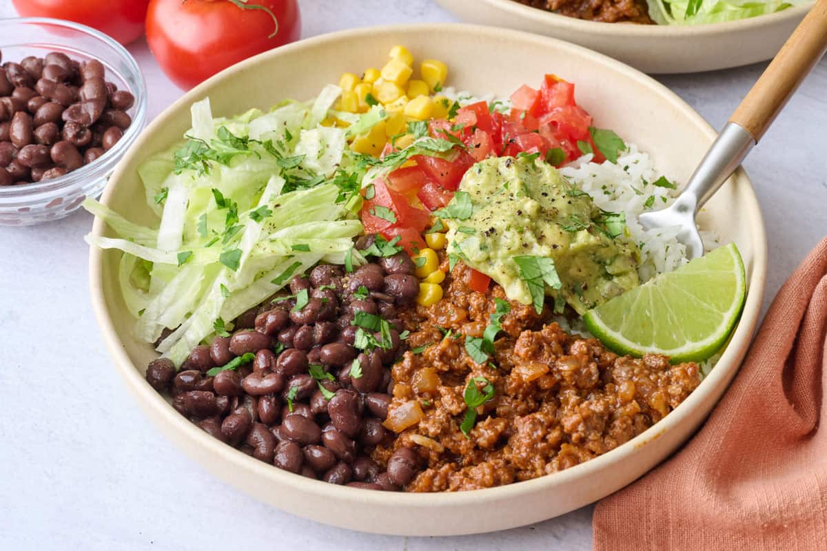 Ground beef burrito bowl with cilantro lime rice, beans, corn, and taco toppings.