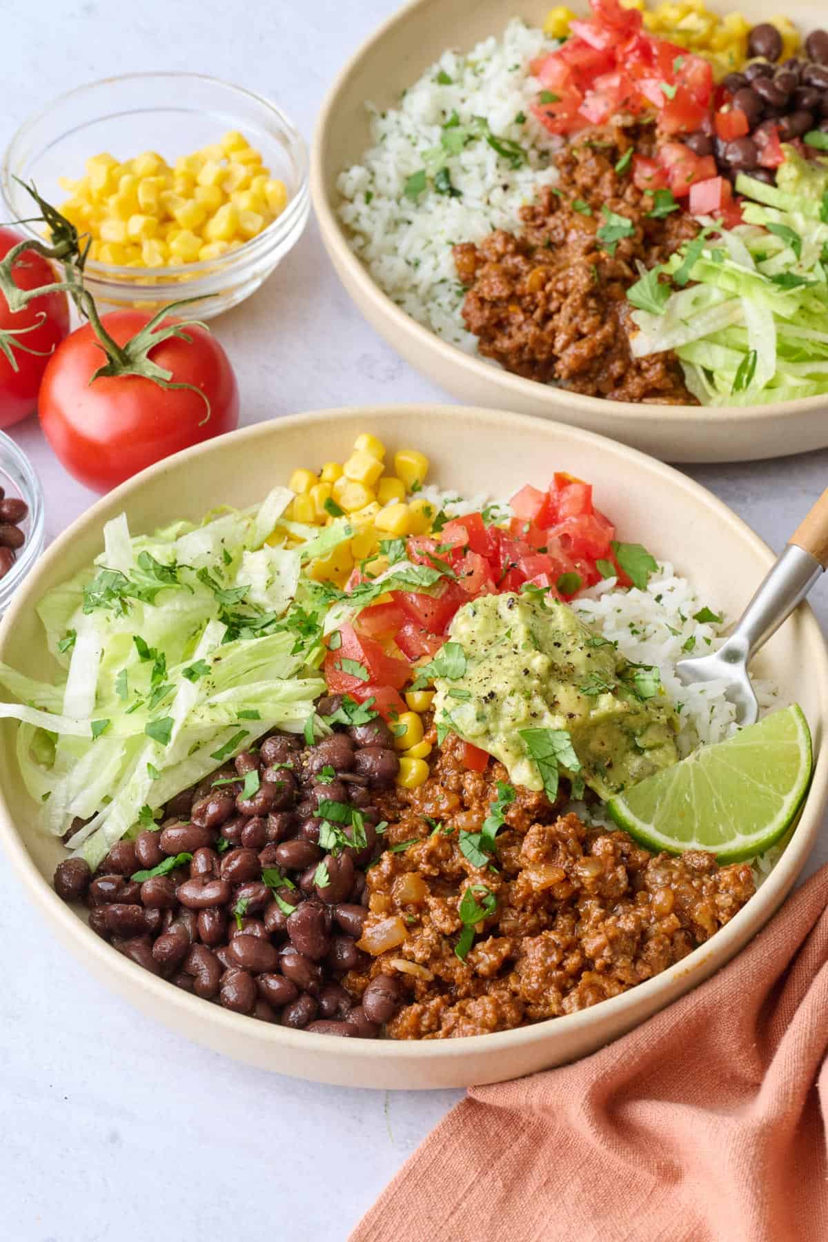 Two beef burrito bowls with rice, beans, and extra taco toppings.