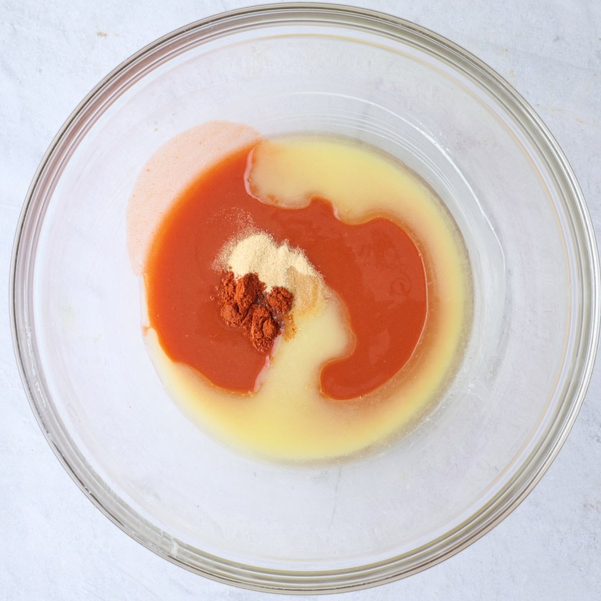 Melted butter, hot sauce, garlic powder and paprika in a bowl before mixing.