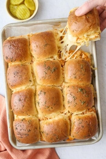 Easy buffalo chicken sliders on a baking sheet with one piece being grabbed with a cheesy pull.