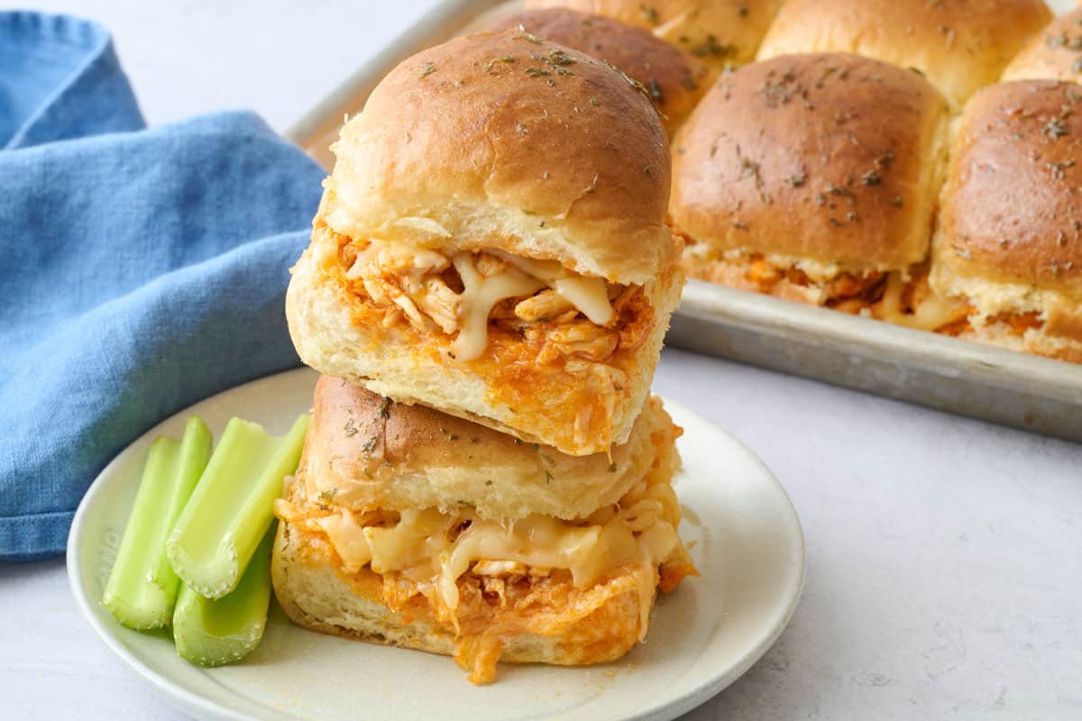 Two cheesy shredded buffalo chicken sliders on a plate with more nearby.