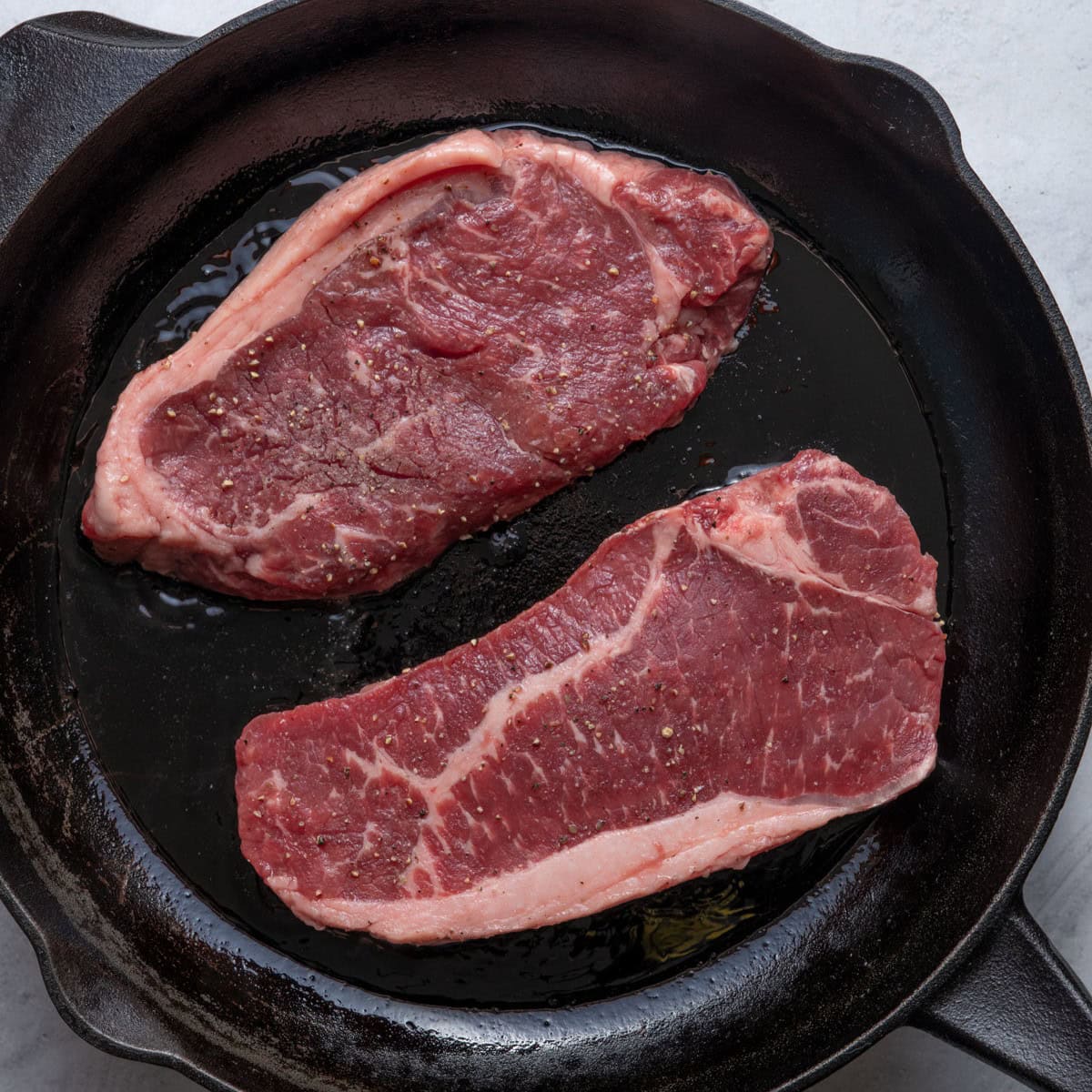 Seasoned steaks added to an oiled cast iron skillet.
