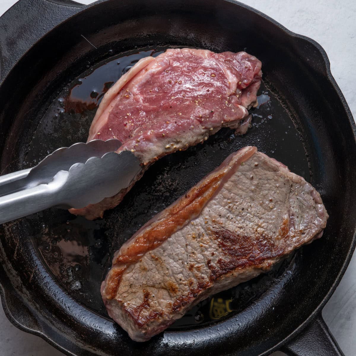 Steaks after searing one side being flipped over in pan.