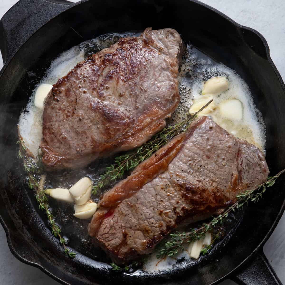Skillet steaks after cooking with butter, garlic and herbs added to pan.