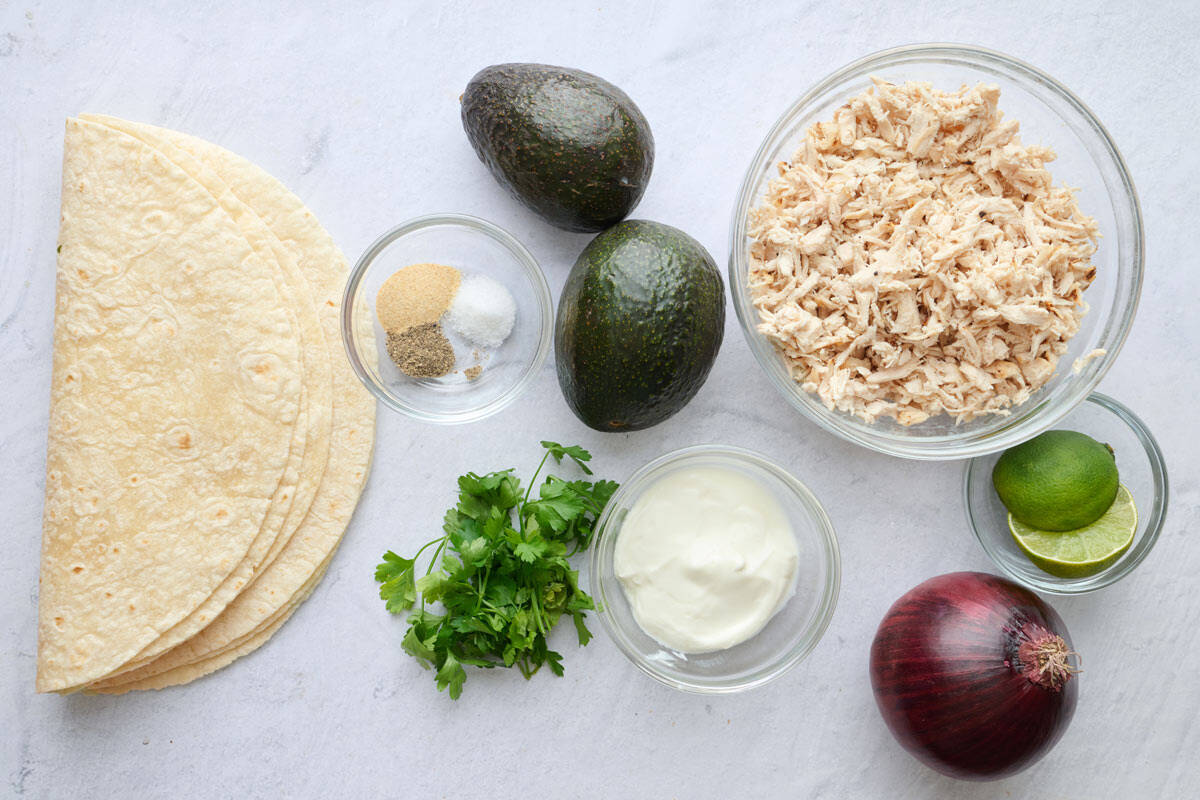 Ingredients for wrap recipe: flour tortillas, seasonings, avocado, parsley, yogurt, shredded chicken, lime, and red onion.