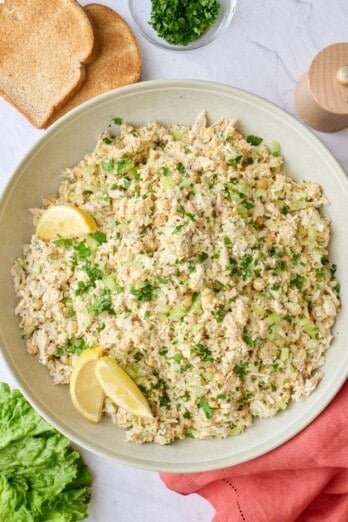 Easy chicken chickpea salad in a serving bowl garnished with chopped parsley and lemon wedges.