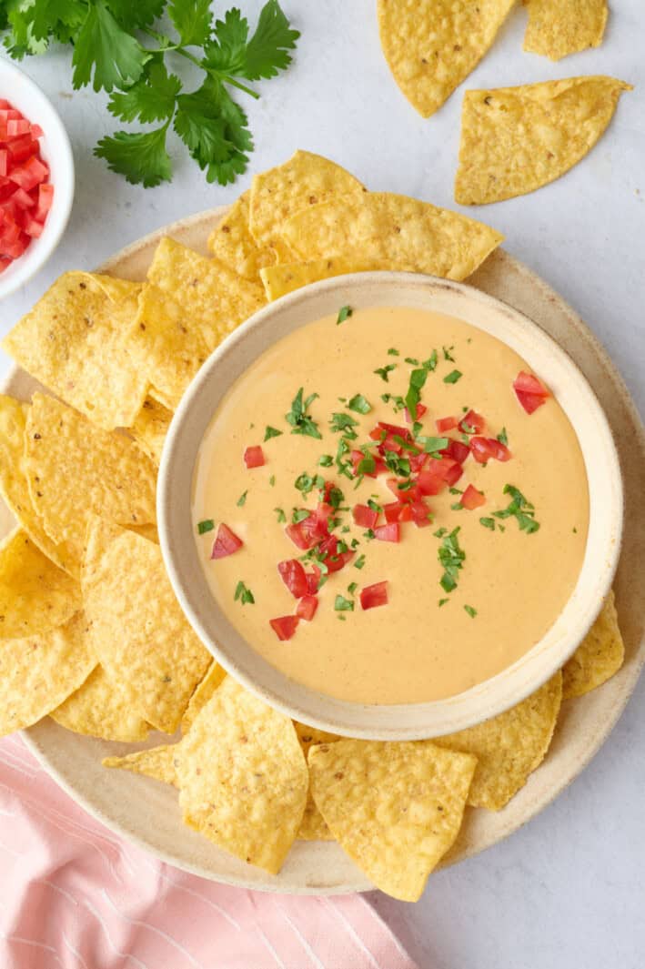 High protein cottage cheese queso in a serving bowl topped with chopped tomato and cilantro and served with tortilla chips.