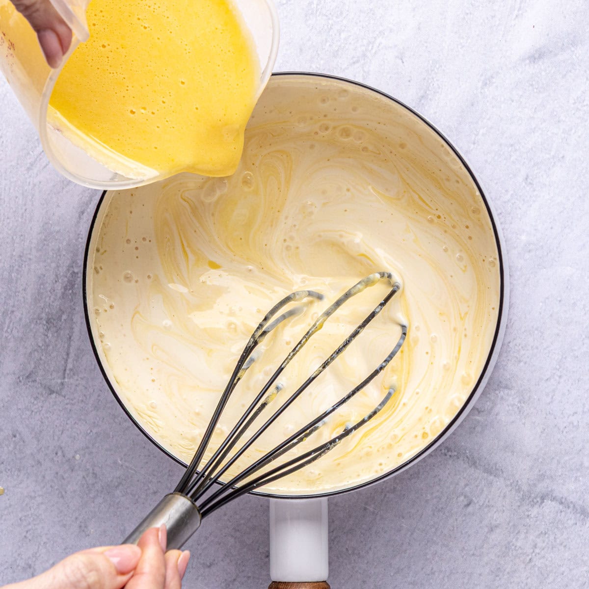 Tempered egg mixture being whisked into remaining warmed milk.