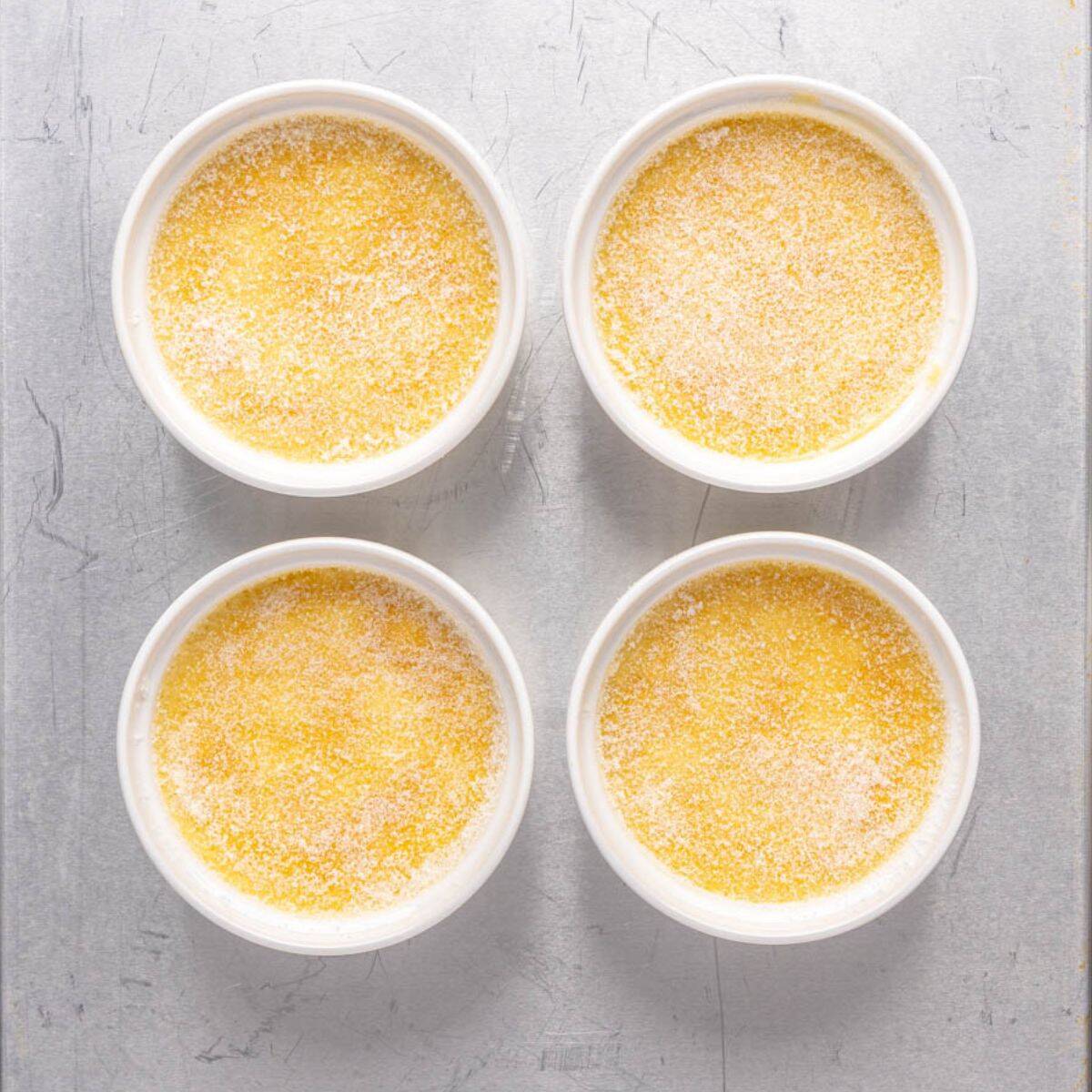 Chilled custard in ramekins on a sheet pan with sugar sprinkled on top before caramelizing.
