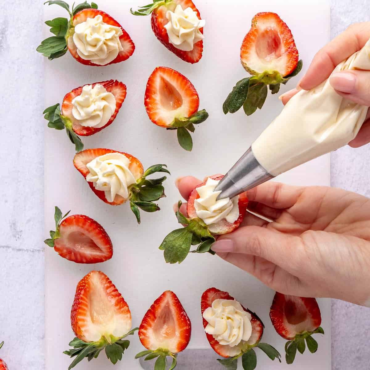No bake cheesecake filling being piped into fresh strawberries cut in half.