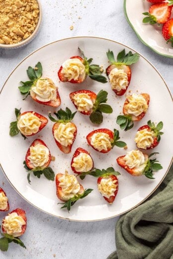 No-bake cheesecake deviled strawberries on a platter with extra crushed graham crackers nearby.