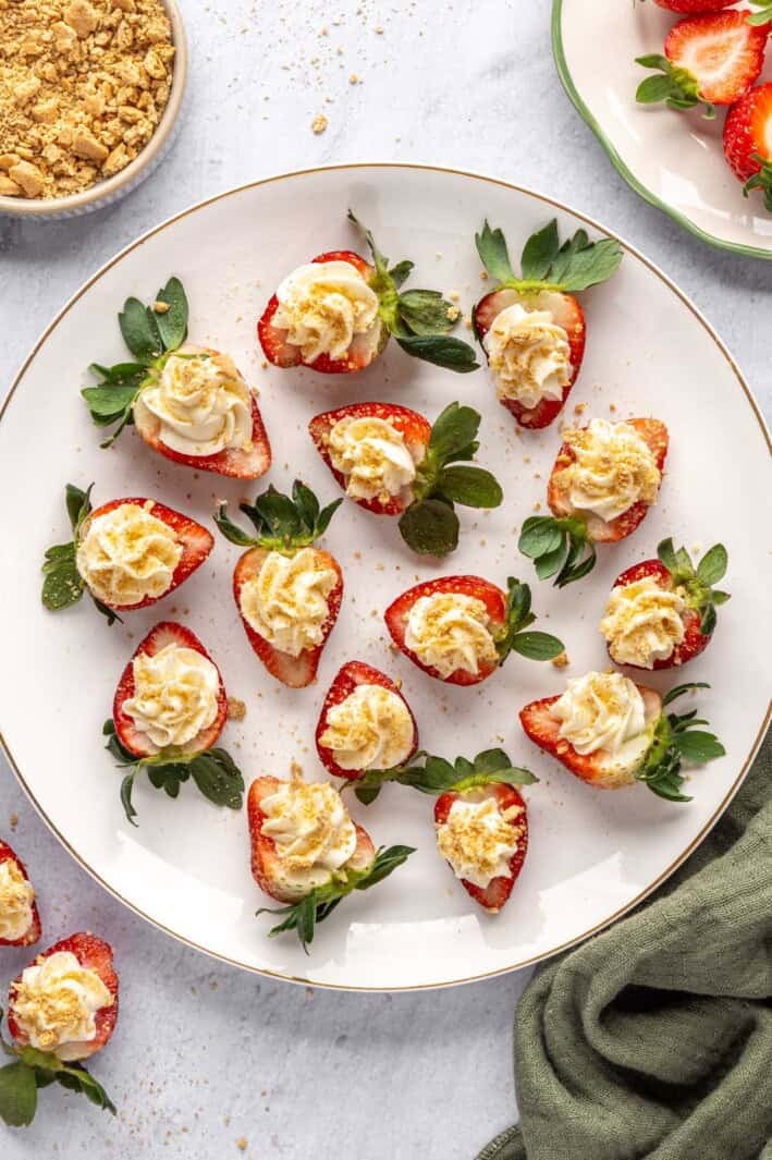 No-bake cheesecake deviled strawberries on a platter with extra crushed graham crackers nearby.