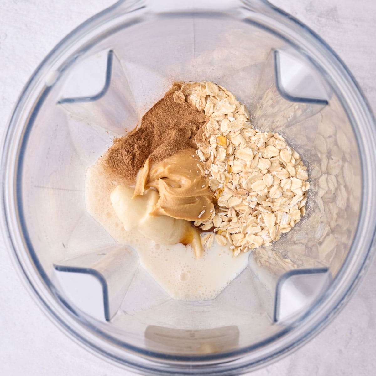 Oats, peanut butter, milk, banana, cinnamon, and maple in a blender before blending.