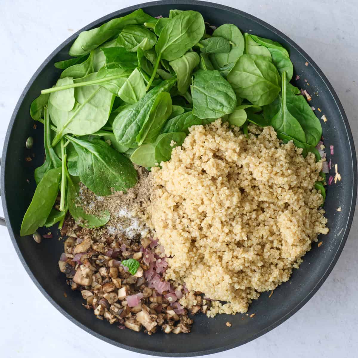 Cooked onions and mushrooms in a large skillet with cooked quinoa, spinach and seasonings added before combining.