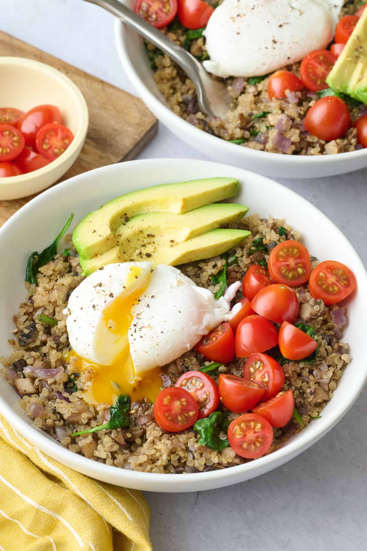 Poached egg served over a bowl of spinach and mushroom quinoa with tomatoes and avocado on top for a healthy breakfast bowl.