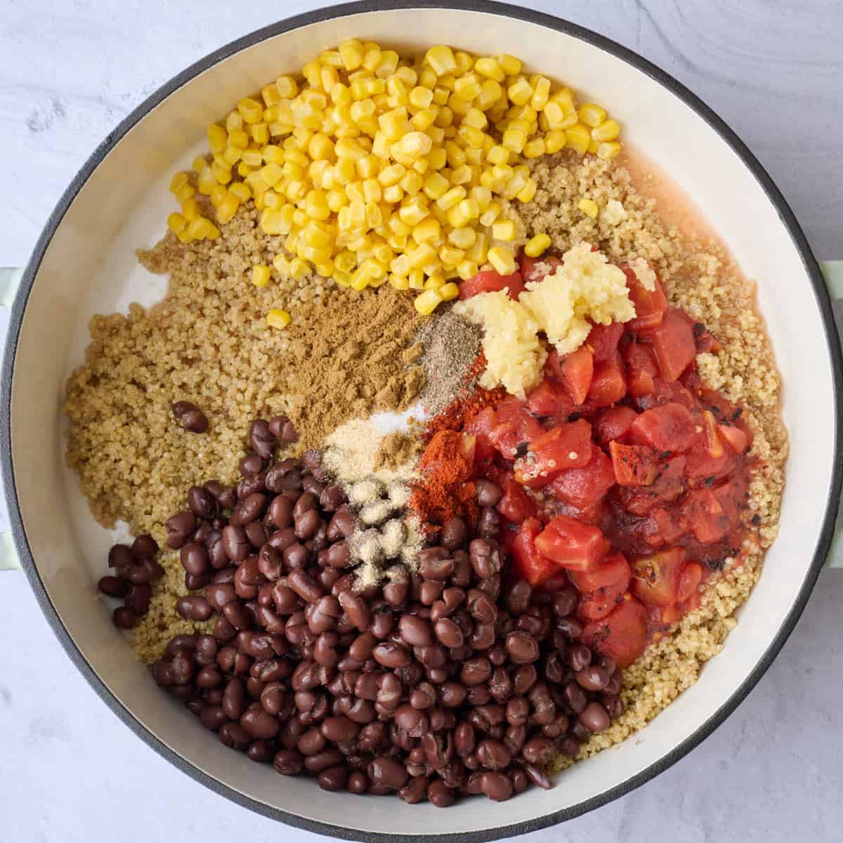 Quinoa after cooking in a large skillet with garlic, tomatoes, black beans, and seasonings added before combining.