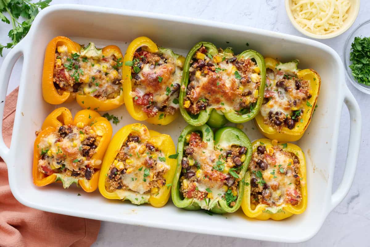 Vegetarian Mexican stuffed peppers recipe in a baking dish filled with quinoa, corn, beans and topped with cheese.