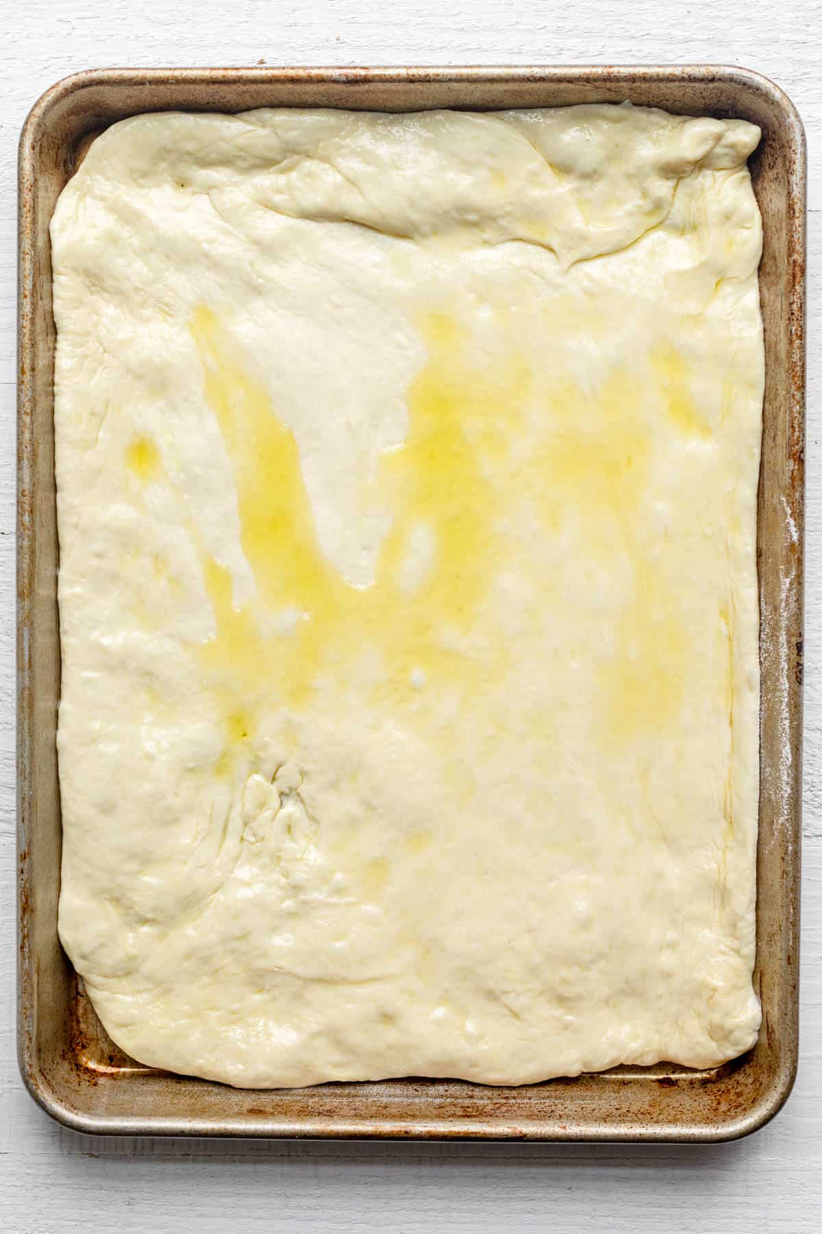 Pizza dough stretched into a sheet pan and coated with oil.