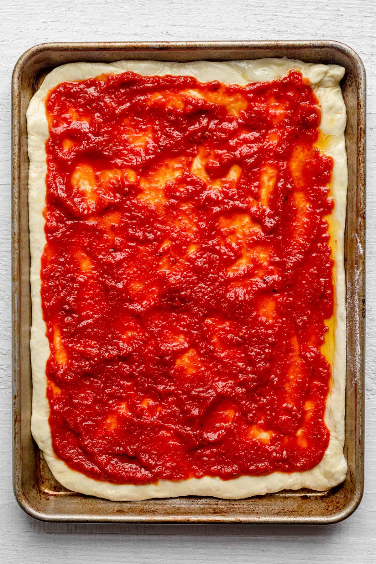 Pizza sauce spread of dough on a sheet pan.