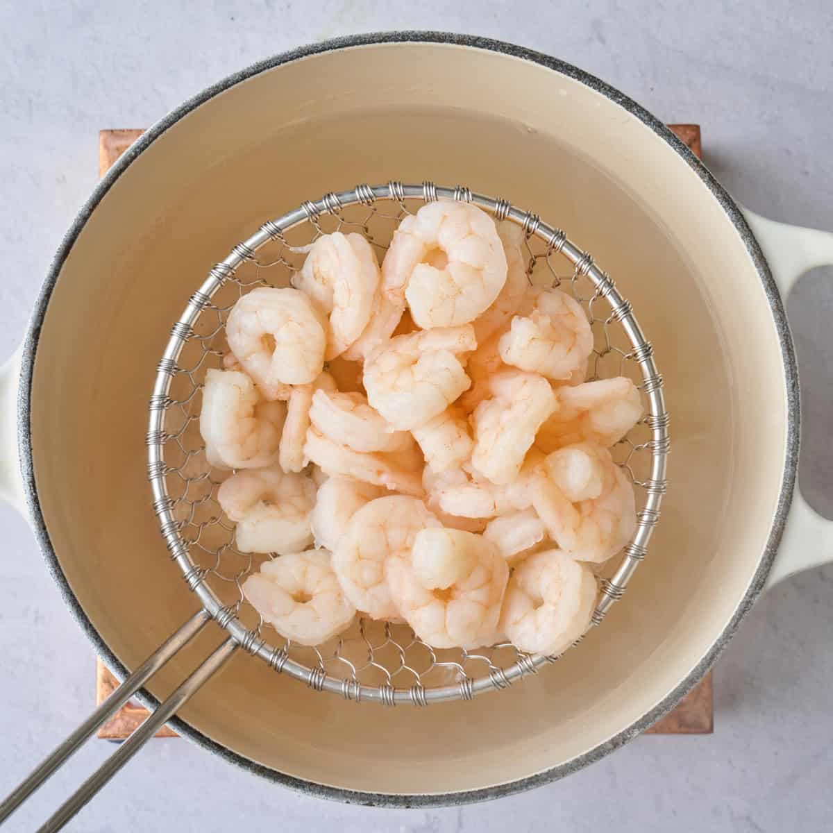 Shrimp being lifted out of water with a spider ladle after bright pink and cooked.