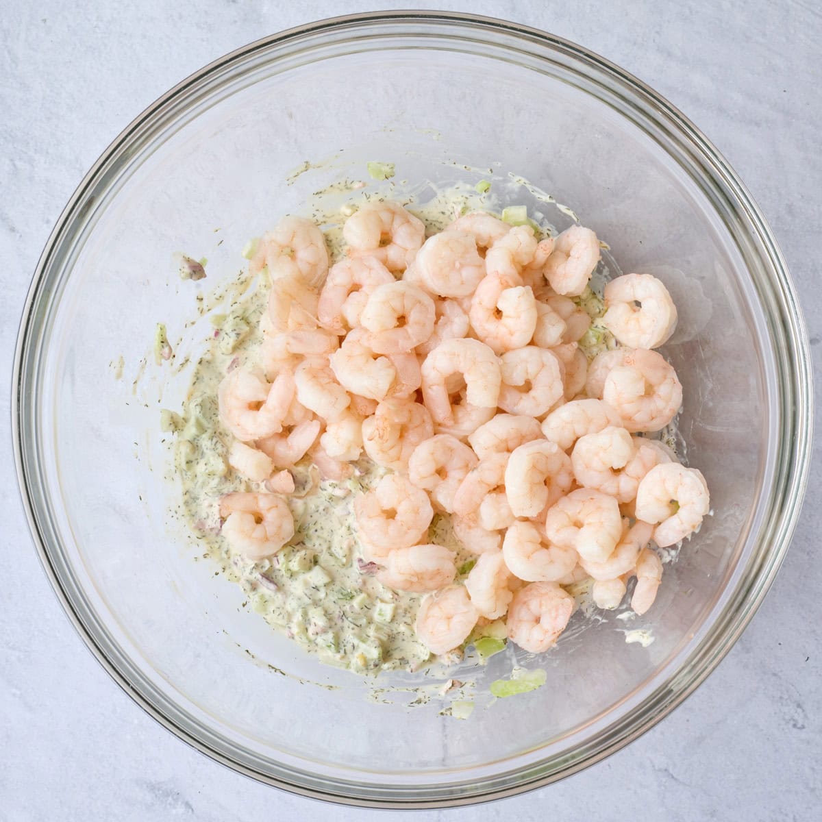 Small cooked shrimp added on top of salad dressing with chopped veggies before tossing together.