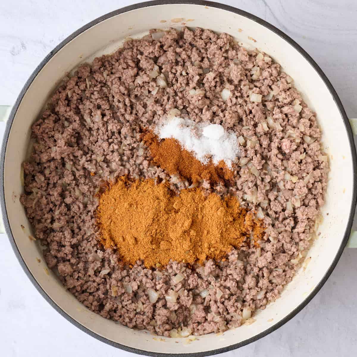 Ground beef and onions in pot after browned with garlic and seasonings added before combining.