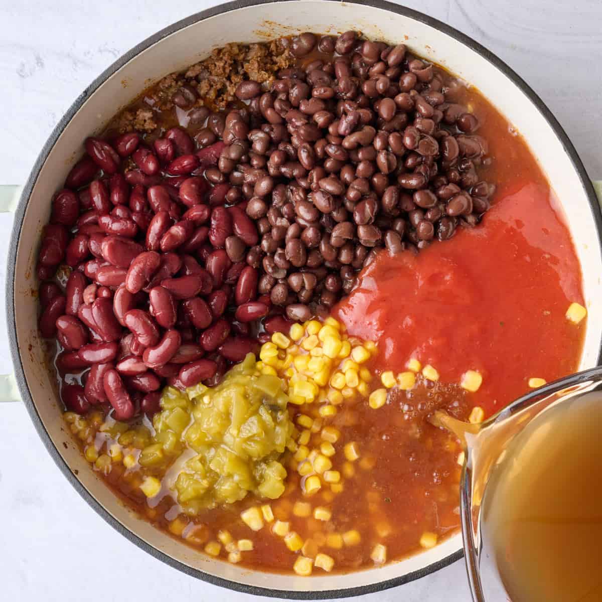 Beans, tomato sauce, corn, chiles and broth added to cooked ground beef and onions for soup recipe.