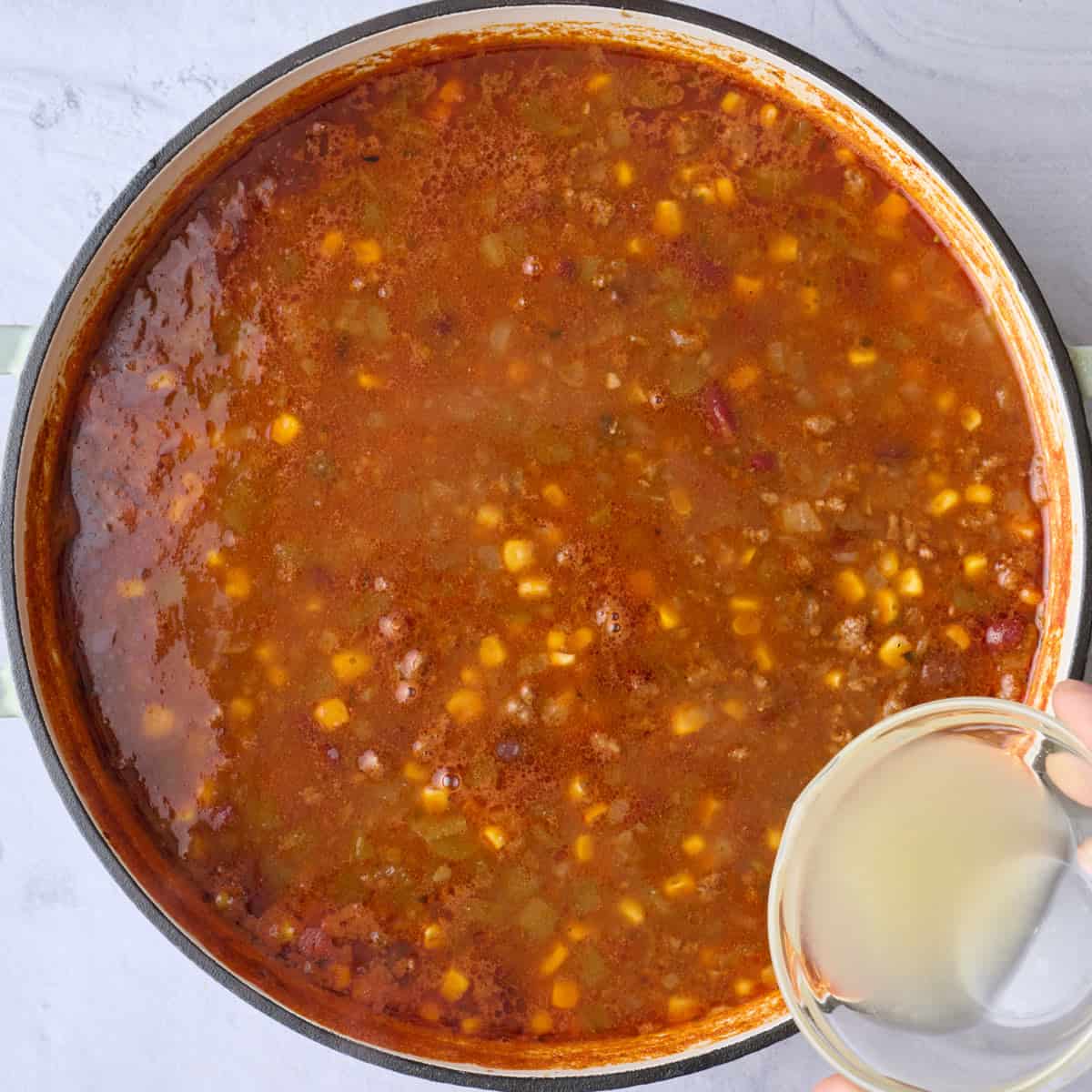Taco soup with beef and beans after cooking with lime juice being poured into pot.
