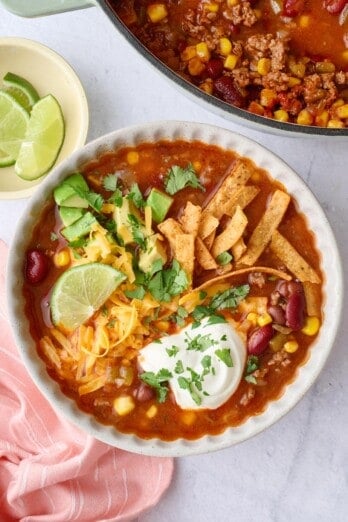 Easy taco soup recipe served in a bowl garnished with cheese, sour cream, avocado, tortilla strips, and cilantro.