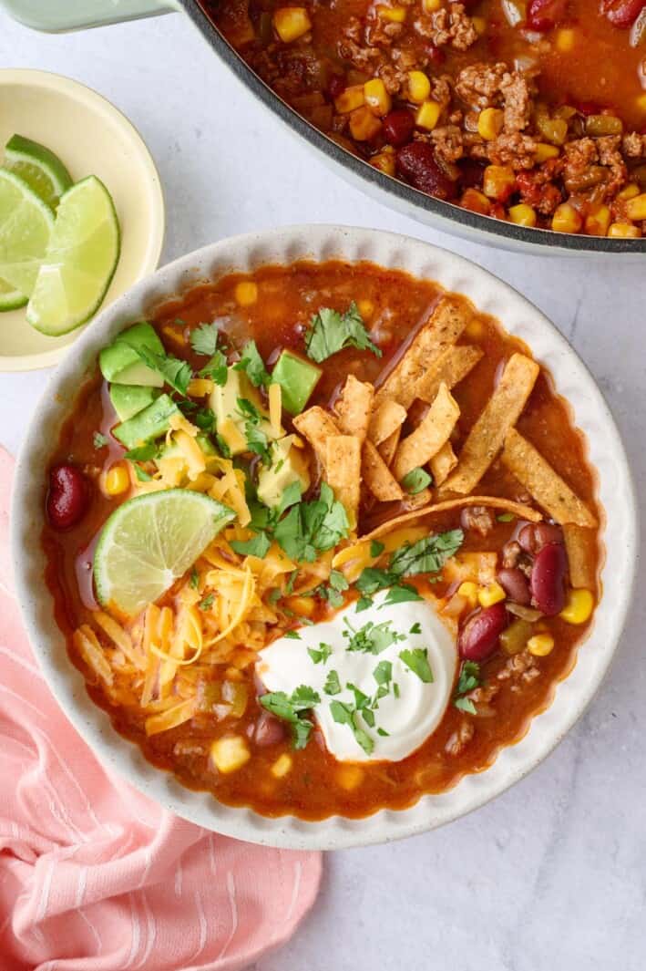 Easy taco soup recipe served in a bowl garnished with cheese, sour cream, avocado, tortilla strips, and cilantro.
