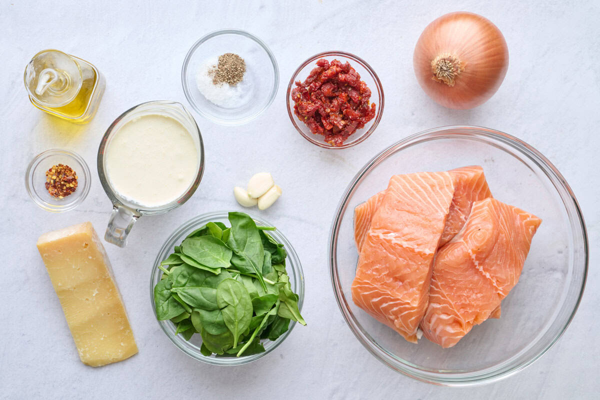 Ingredients for Tuscan salmon recipe: oil, red pepper flakes, parmesan cheese, cream, salt and pepper, sun dried tomatoes, garlic cloves, spinach, onion, and salmon fillets.