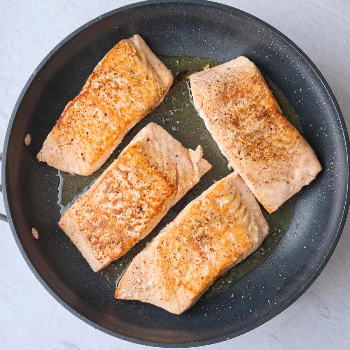 Cooked salmon after flipping in a skillet to show golden flesh.