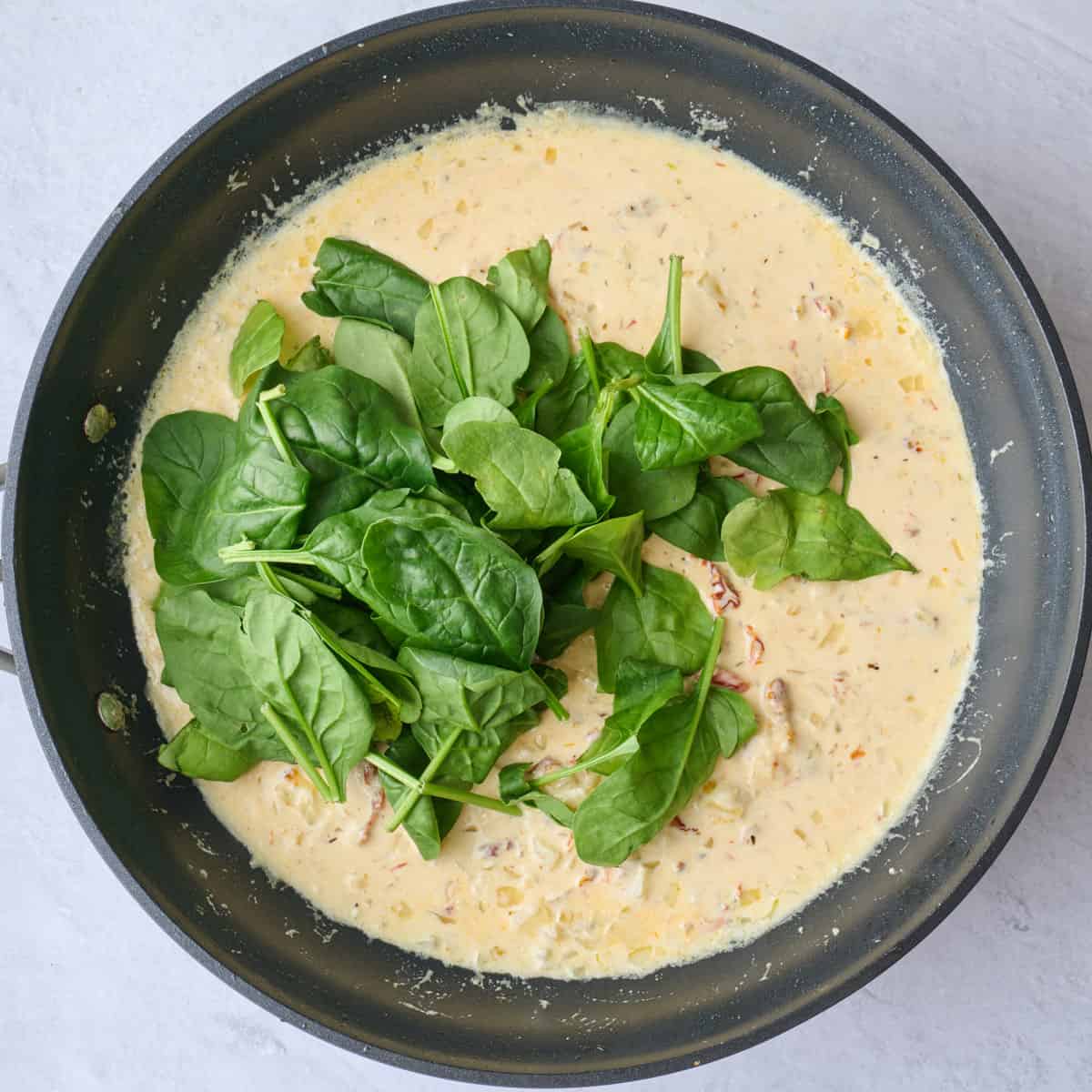 Spinach added to creamy tuscan sauce before combining.