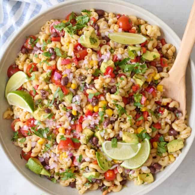 Bean and macaroni pasta salad recipe in a serving bowl garnished with cilantro and lime wedges.