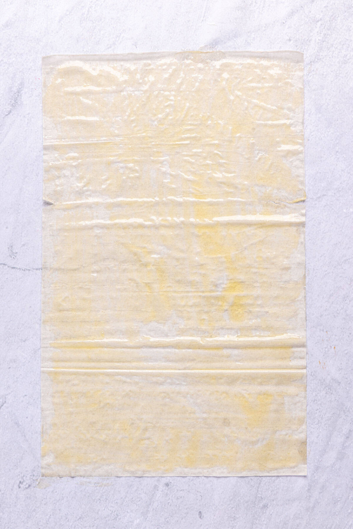 One sheet of phyllo dough on surface after brushing with melted ghee.