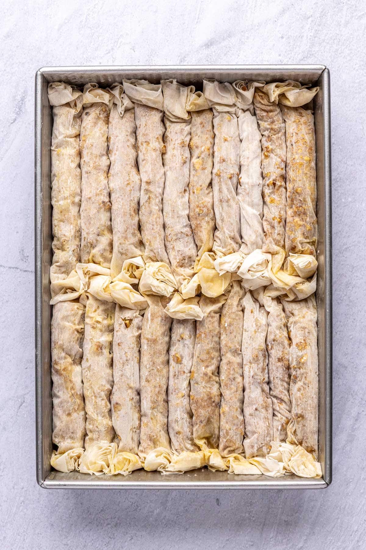 Baking dish with baklava logs rolled and placed seam side down after pushing to create crinkle affect.