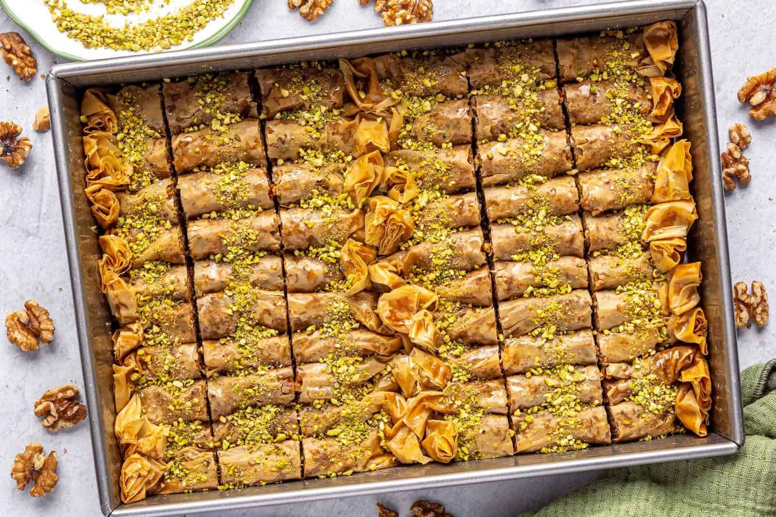 Burma baklava in a baking dish garnished with crushed pistachios and filled with a walnut mixture.