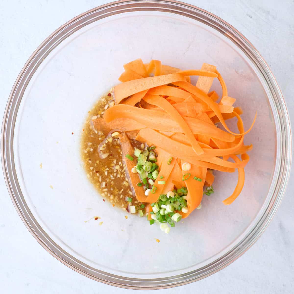 The dressing ingredients in a large bowl after whisking together, with the carrots and green onions added on top.