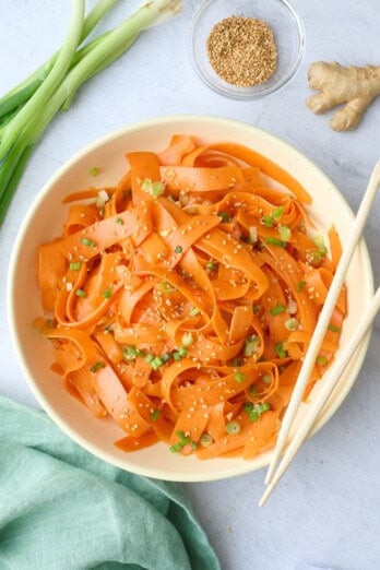 Carrot salad in a serving bowl garnished with sesame seeds, chopsticks dipped inside, small dish of extra sesame seeds nearby