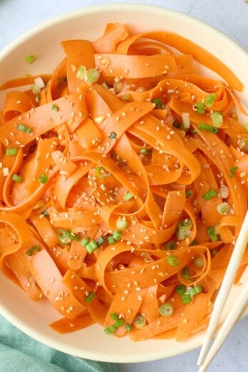 Carrot salad in a serving bowl garnished with sesame seeds, chopsticks dipped inside, small dish of extra sesame seeds nearby