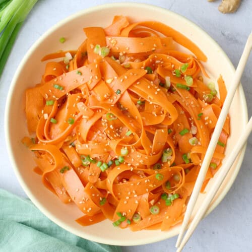 Carrot salad in a serving bowl garnished with sesame seeds, chopsticks dipped inside, small dish of extra sesame seeds nearby