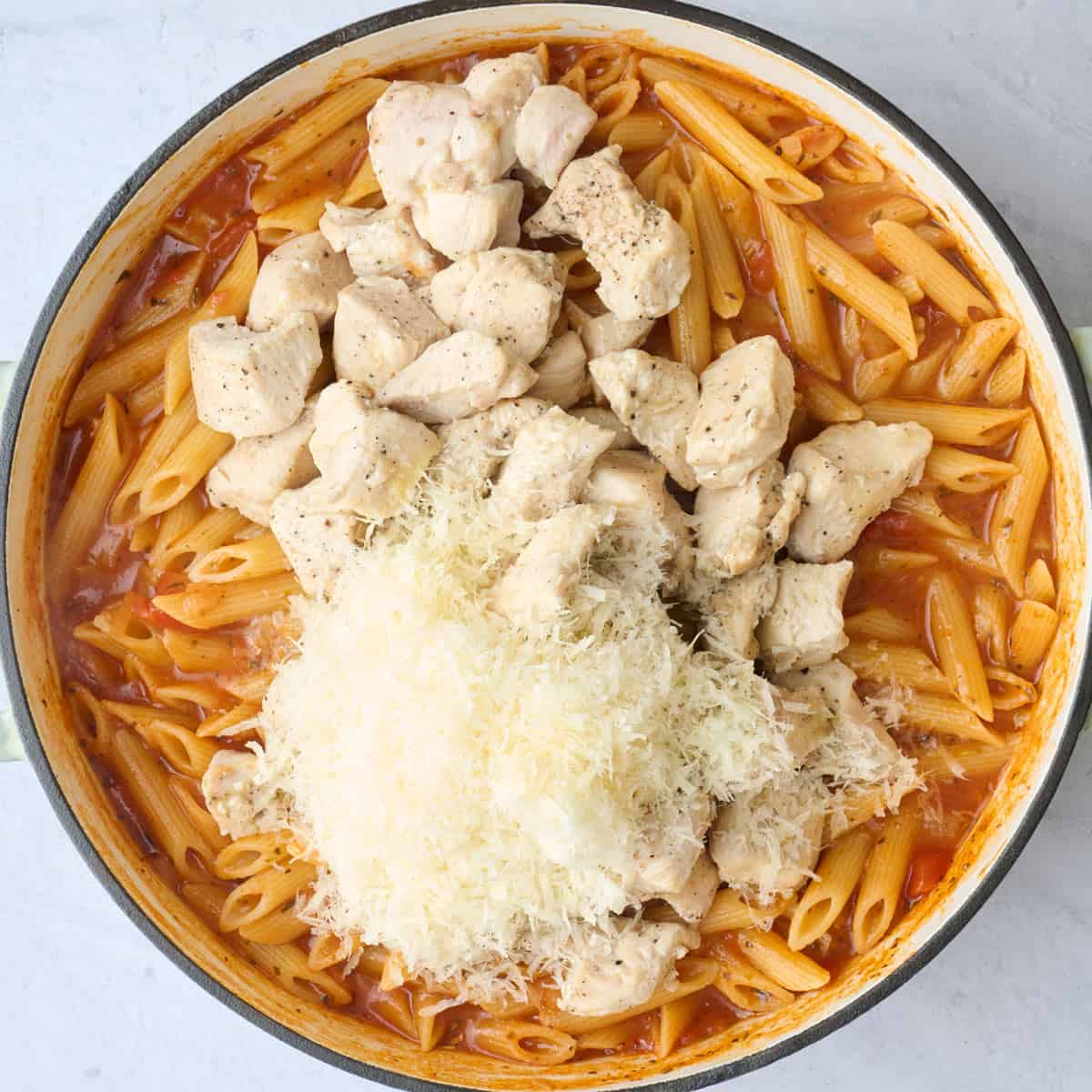 Pot of combined sauce and pasta with the chicken and parmesan added to the top.