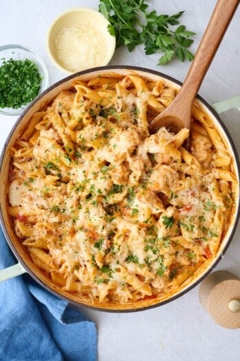 Chicken Parmesan Pasta in a pot with a wooden spoon, with ingredients for the recipe surrounding.