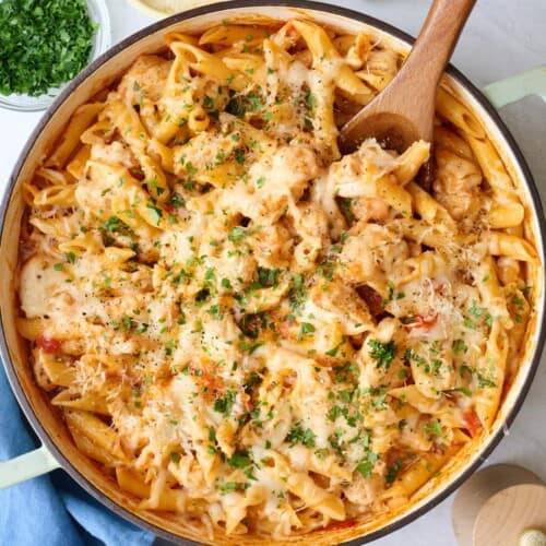 Chicken Parmesan Pasta in a pot with a wooden spoon, with ingredients for the recipe surrounding.