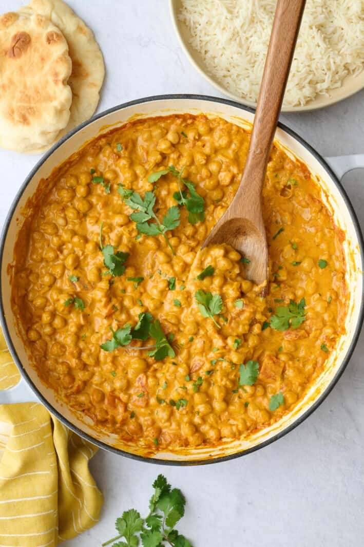 Chickpea curry in the skillet garnished with cilantro, with a dish of basmati rice and naan nearby.