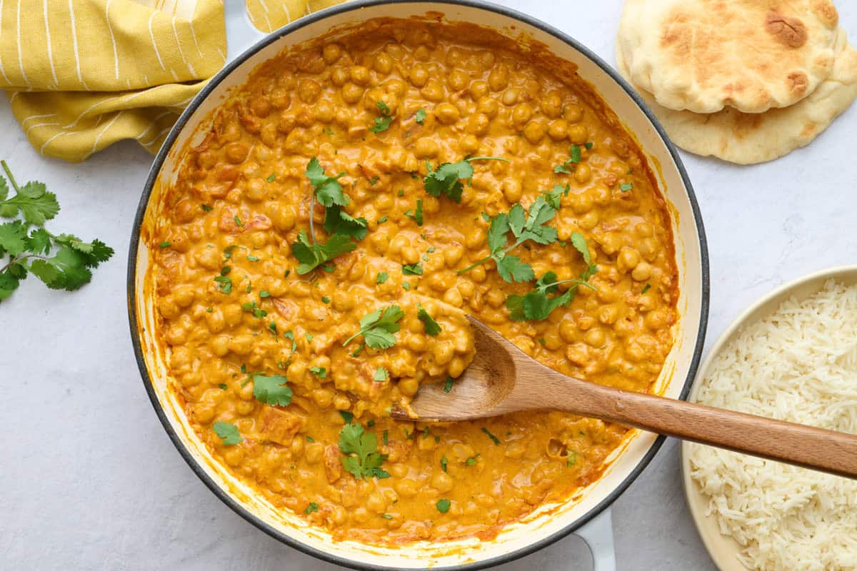 Chickpea curry in the skillet garnished with cilantro, with a dish of basmati rice and naan nearby.