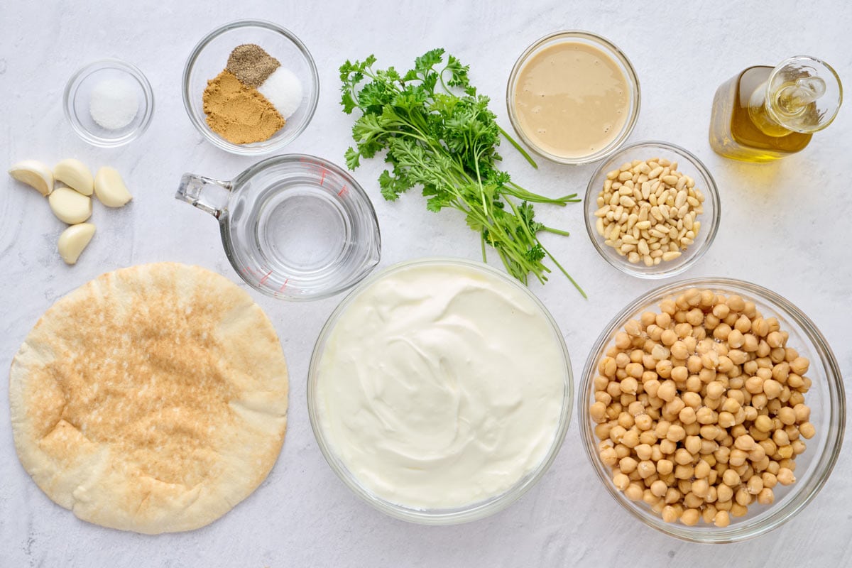 Ingredients for vegetarian lebanese fatteh recipe: pita, garlic, salt, spices, parsley, tahini, pine nuts, yogurt, chickpeas, and oil.