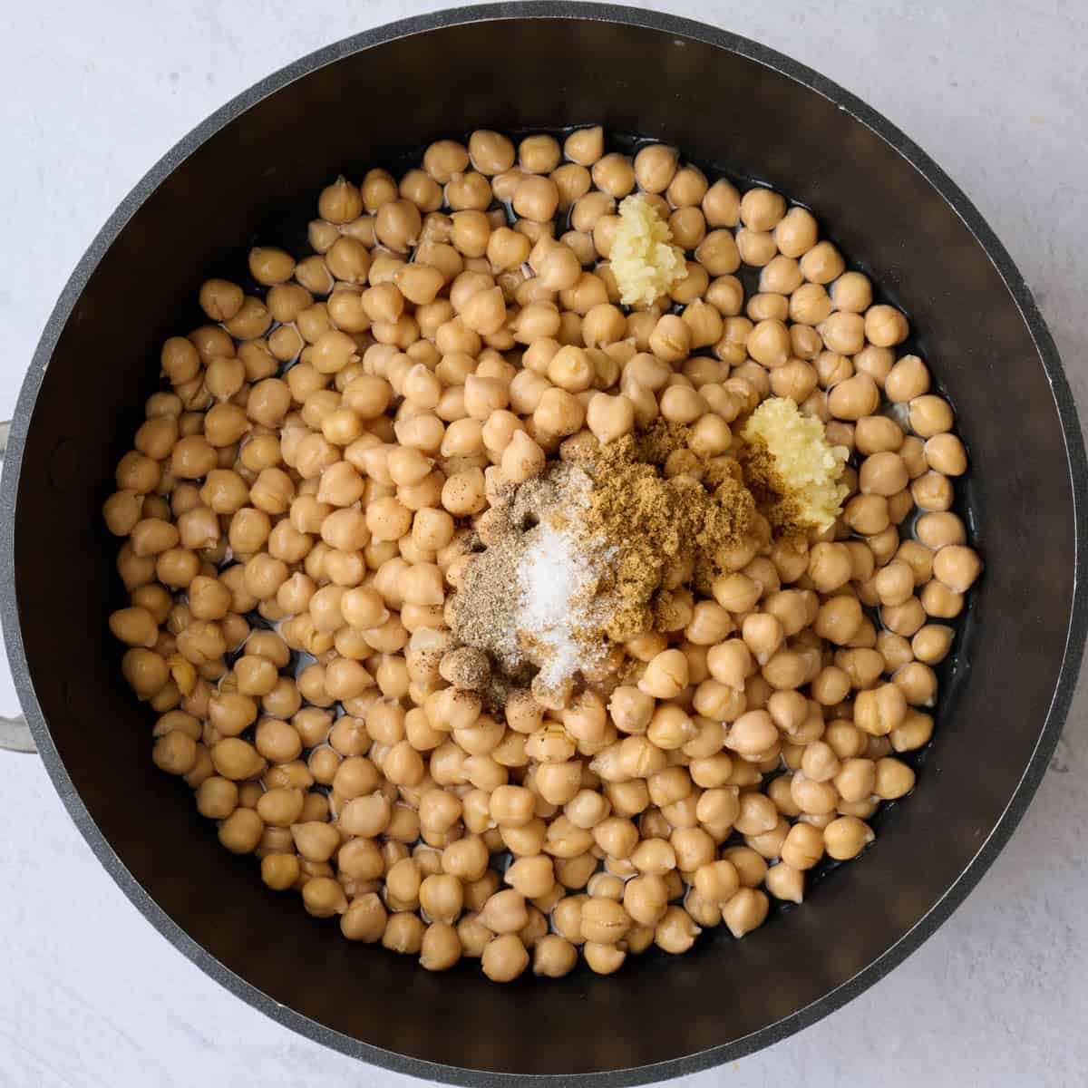 Chickpeas, garlic, cumin, salt and pepper in a pot before cooking.