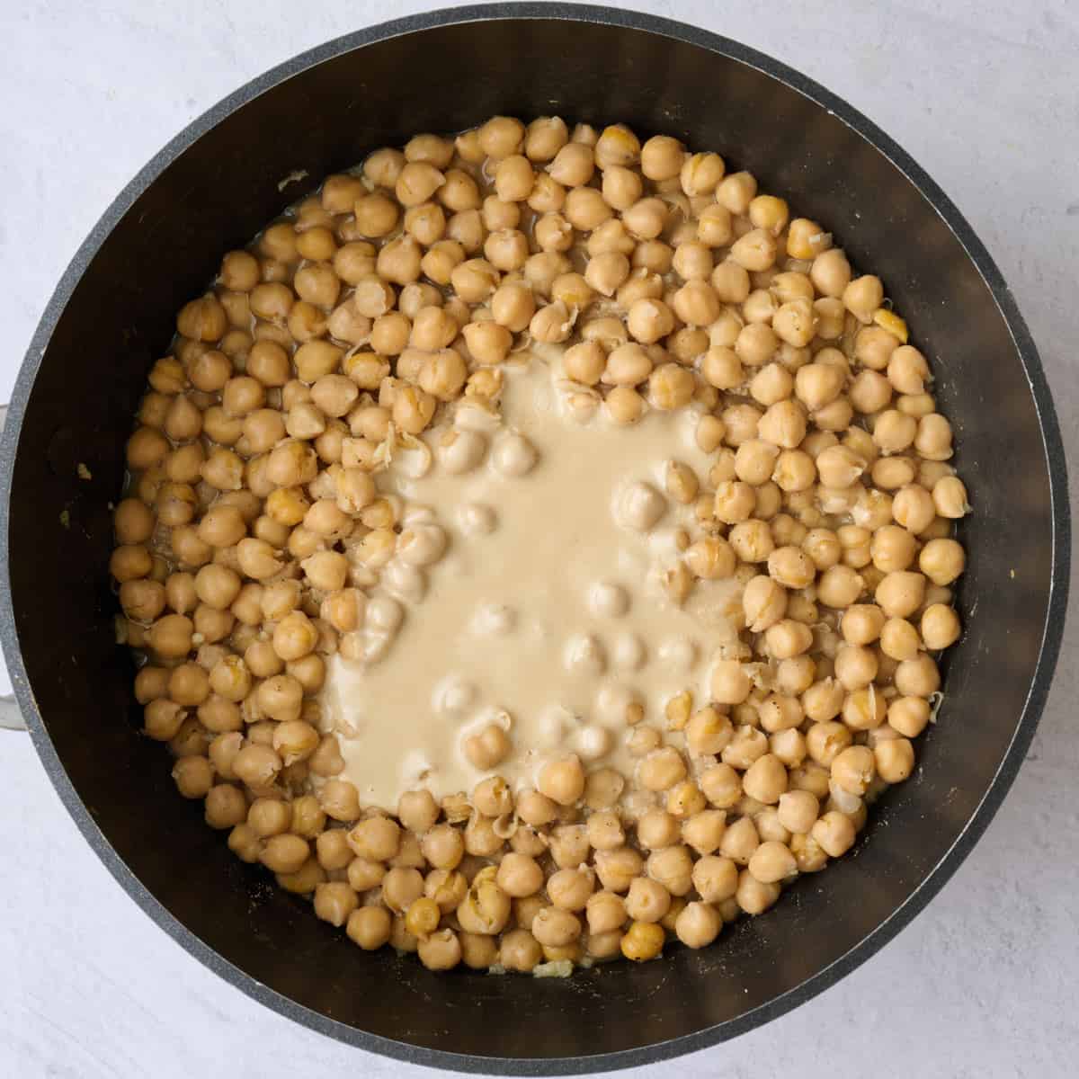 Seasoned chickpeas in a pot after cooking with tahini added on top.